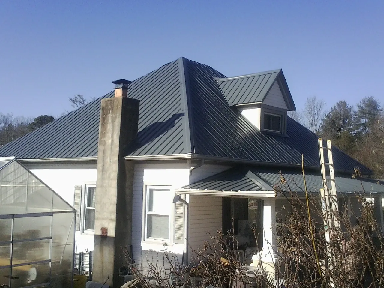 Dark blue standing seam metal roof on a white farmhouse with dormer — Slate & Tile Roof Repair by Roofing Brothers in Sioux Falls