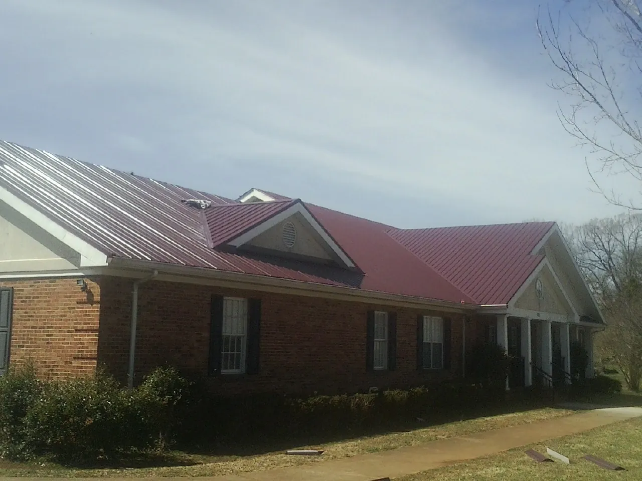 Red metal roof with gabled entries on a long brick building, from a Hail Damage Roof Repair job in Sioux Falls
